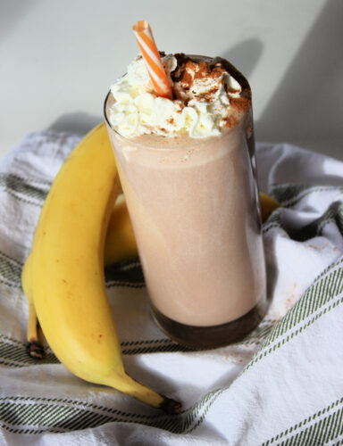 Smoothie in glass with whip cream next to bananas