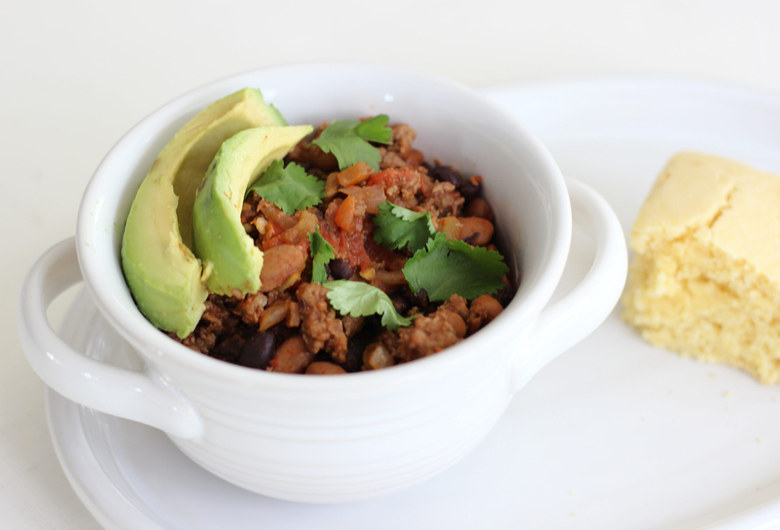 bowl of chili with avocado, cilantro and corn bread